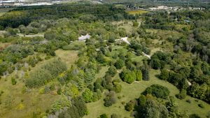 An aerial view of The Arboretum shows many trees and densely wooded areas. A concrete building can be seen nestled between trees.