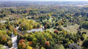 Aerial view of The Arboretum. Autumnal colours are speckled throughout the landscape which is mostly covered in trees.