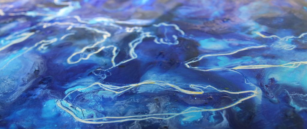 Deep indigo, robins egg, and pale powder blue shades of paint swirl and mix to create the texture of water. On top of this rich blue texture, white lines trace the geographical shape of the great lakes.