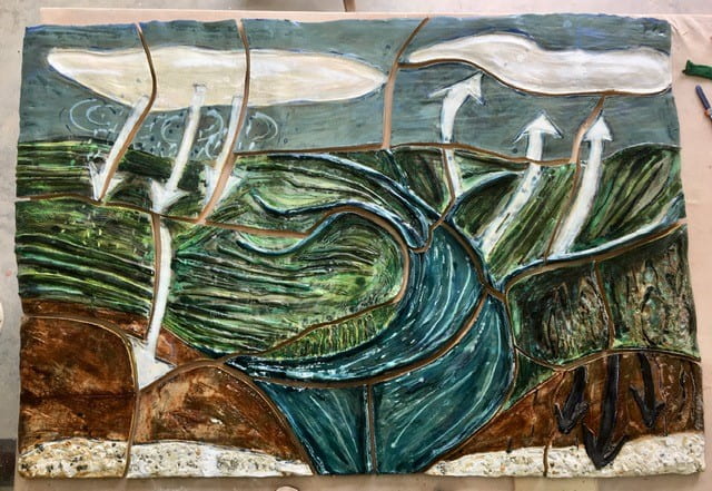A clay sculpture with rough texture shows a blue sky, with arrows moving up and down between the sky, the rolling hills below, and a winding river that cuts through the middle of the image. The scene is broken into multiple pieces but still whole, with the shattered clay fitted back together to make this scene.  